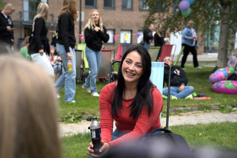 Rødkledd student i hage med andre studenter.